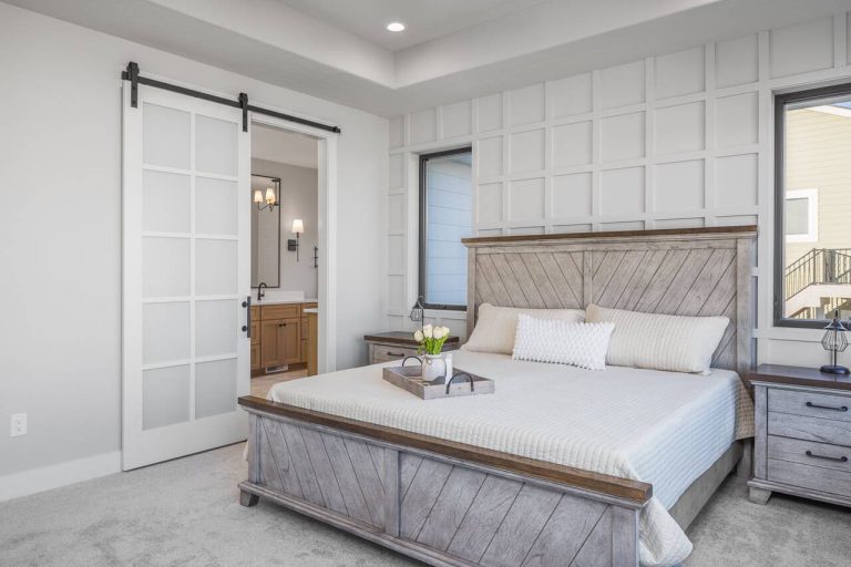 Modern bedroom with a wooden bed, two nightstands, and a sliding barn door leading to a bathroom.