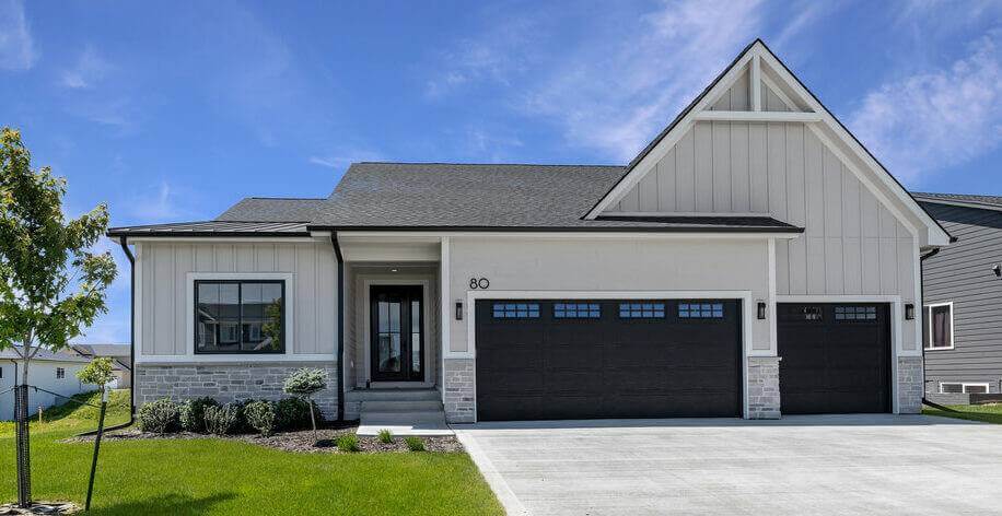 A light-colored custom home that incorporates stonework on the exterior and features a three-car garage